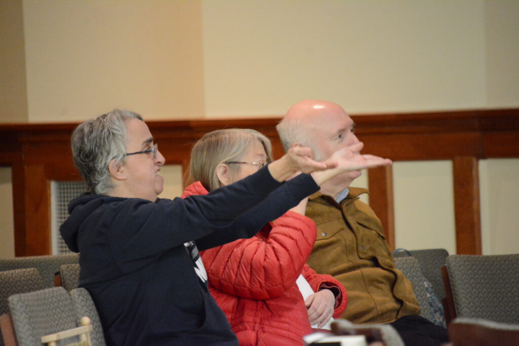 Three members of Sunday Fellowship sit together. One holds her arms out in front of her lifting up a prayer