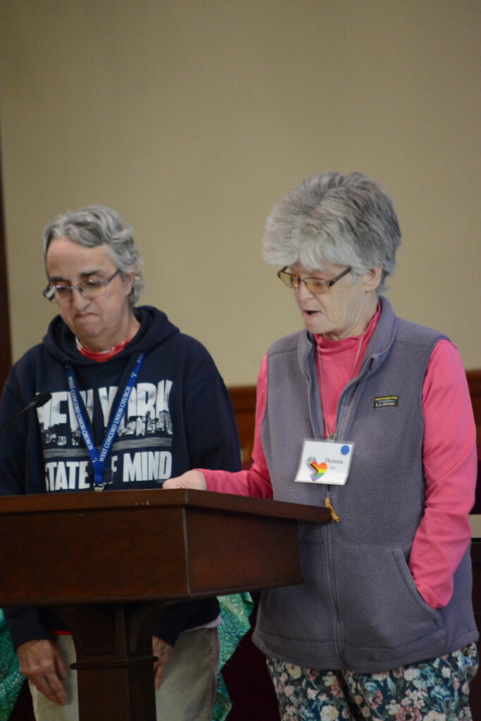 Two women stand at a wooden podium sharing a scripture reading. 